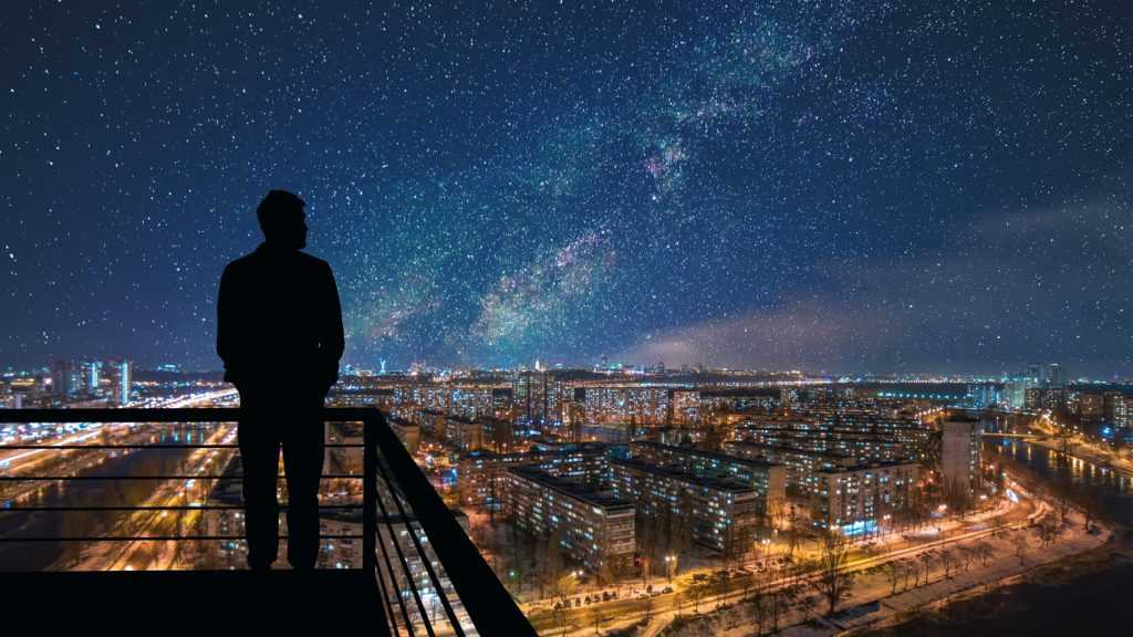 Silhouette of man standing on the top of building on the starry cityscape background